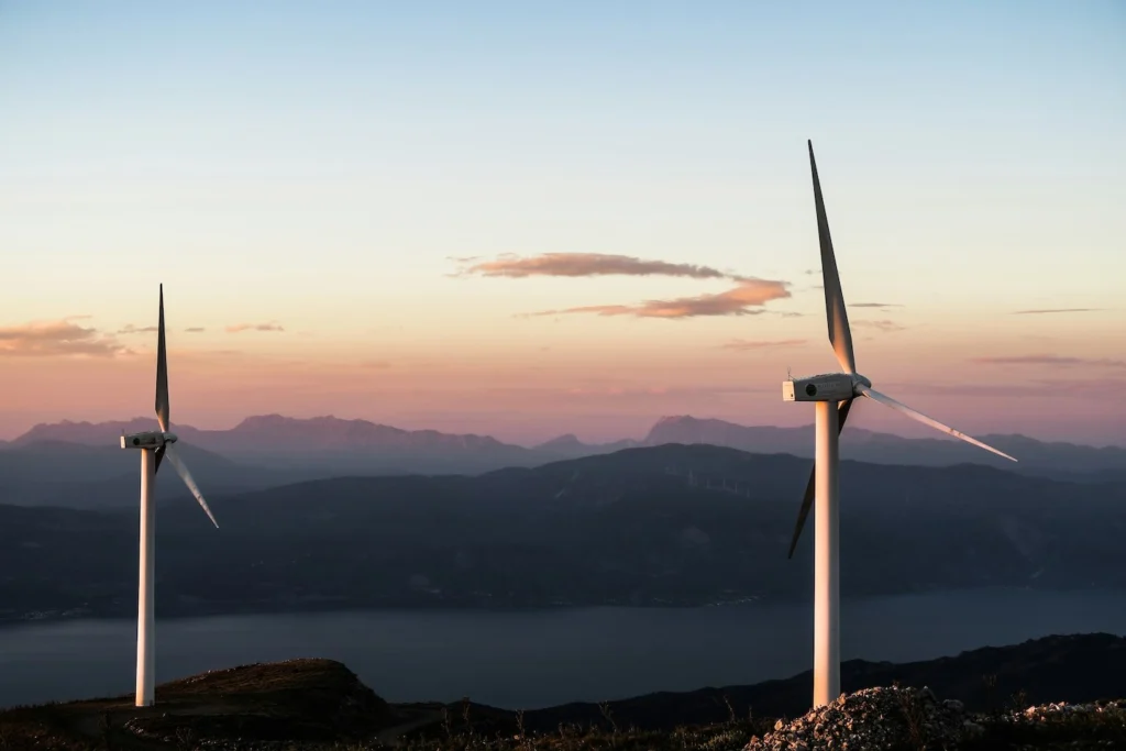 Wind turbines on mountains near water with sunset in background.