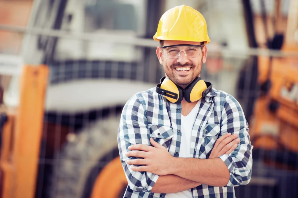 Smiling contractor wearing blue and white plaid shirt and yellow hard hat.