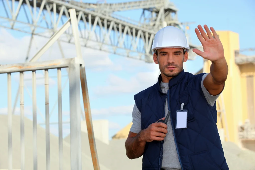 Construction site manager wearing hard hat, holding walkie talkie, hold hand as a gesture to stop.