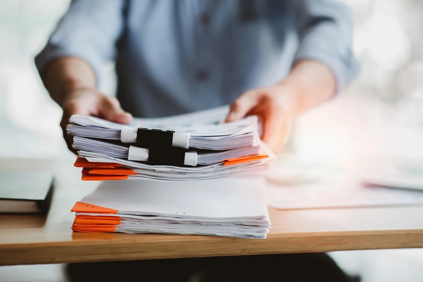 Person placing stack of papers on top of a desk.