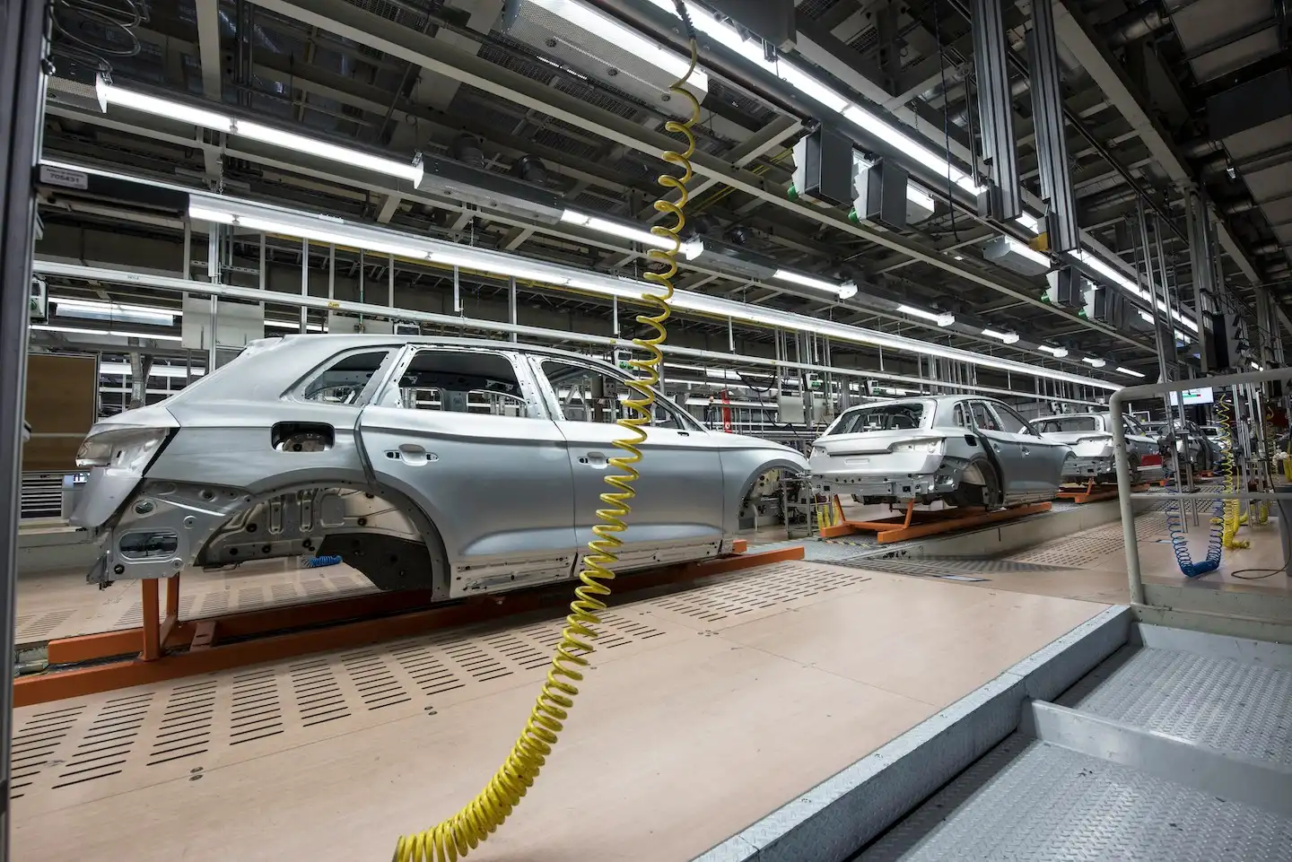 Silver car body skeleton with doors on auto manufacturing line.