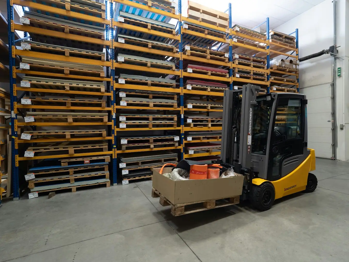 Forklift in manufacturing warehouse with pallet containing a box with miscellaneous items.