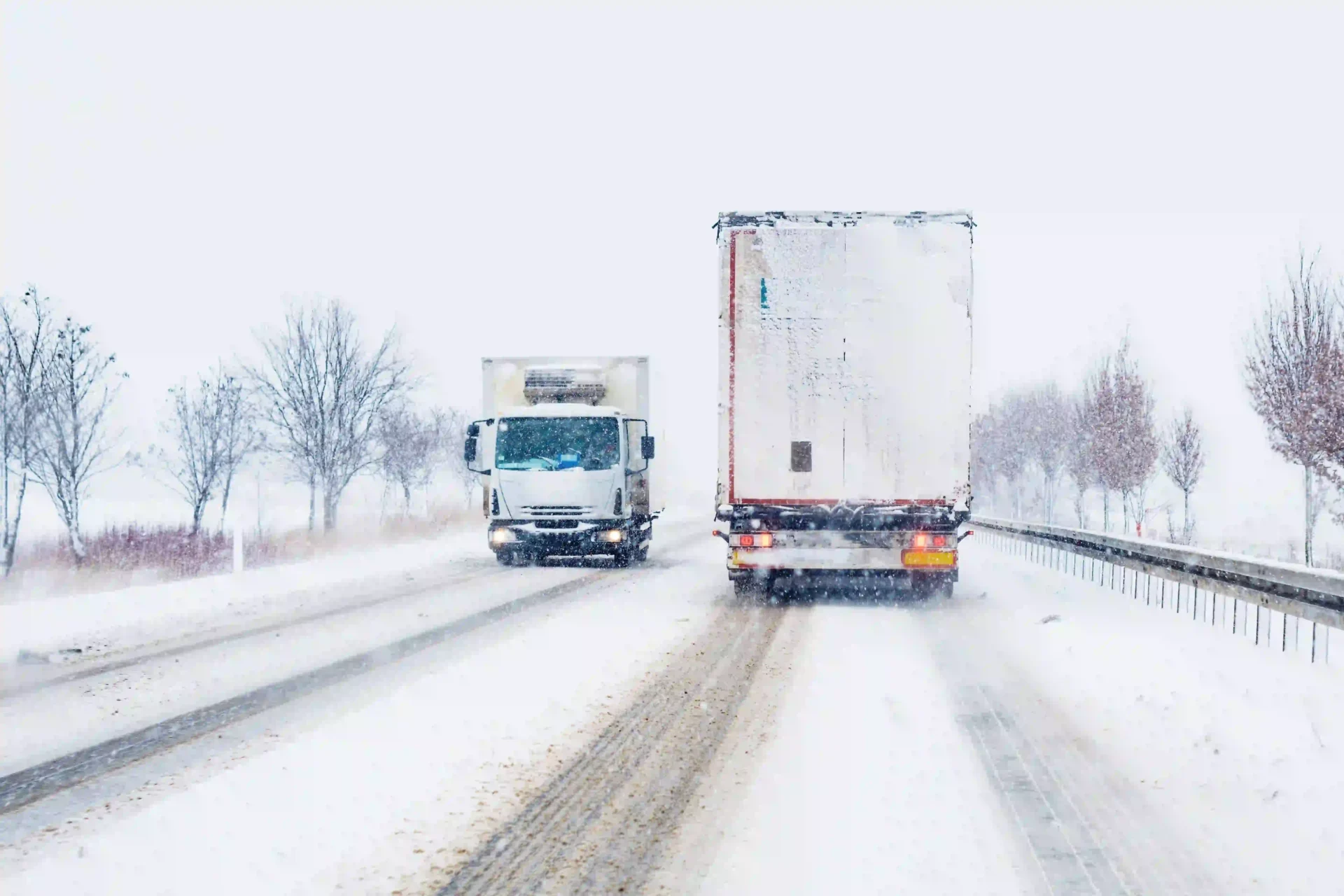 Two semi trucks on a snowy highway moving in opposite directions.