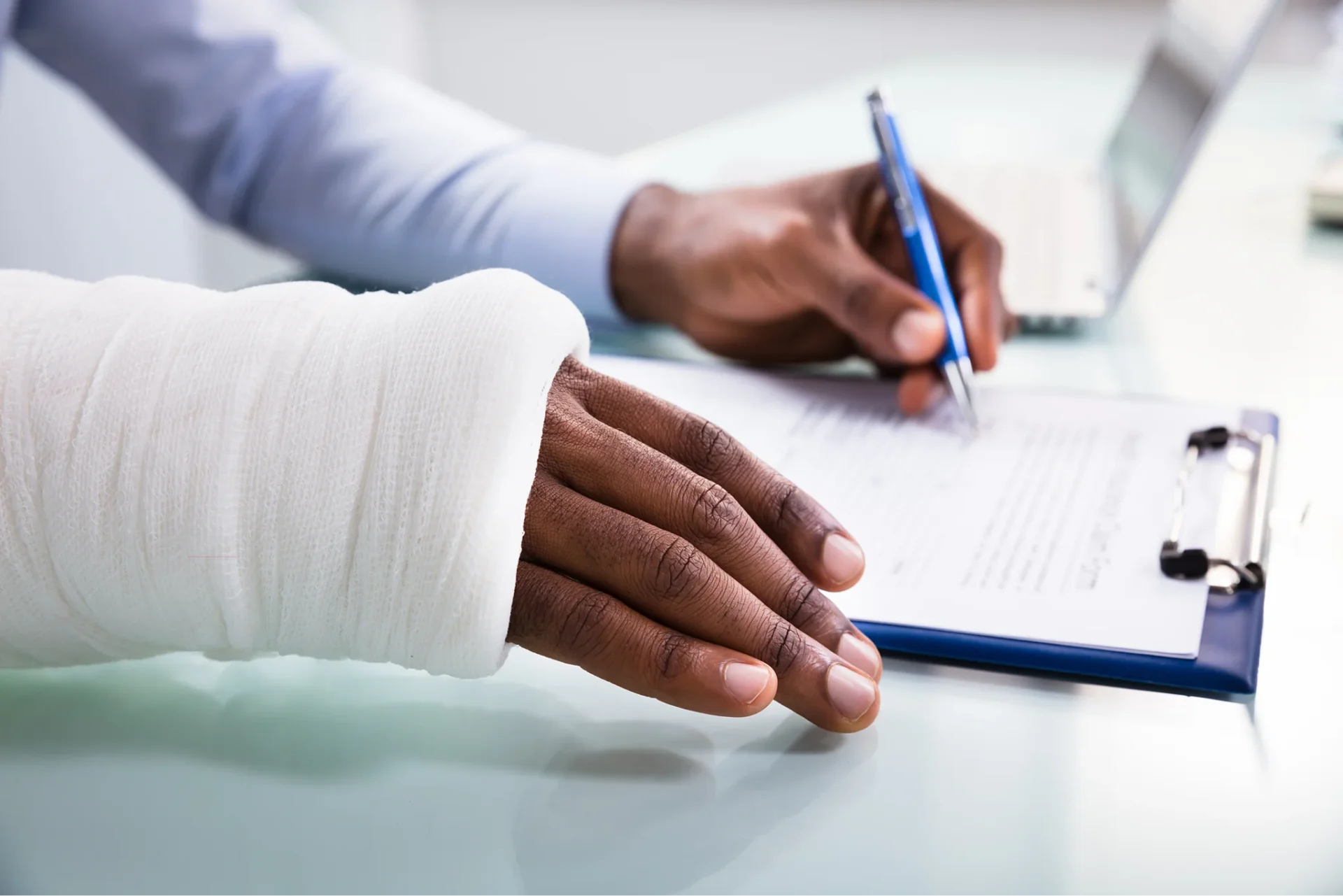 Person with gauze cast on right hand uses left hand to sign workers’ compensation.