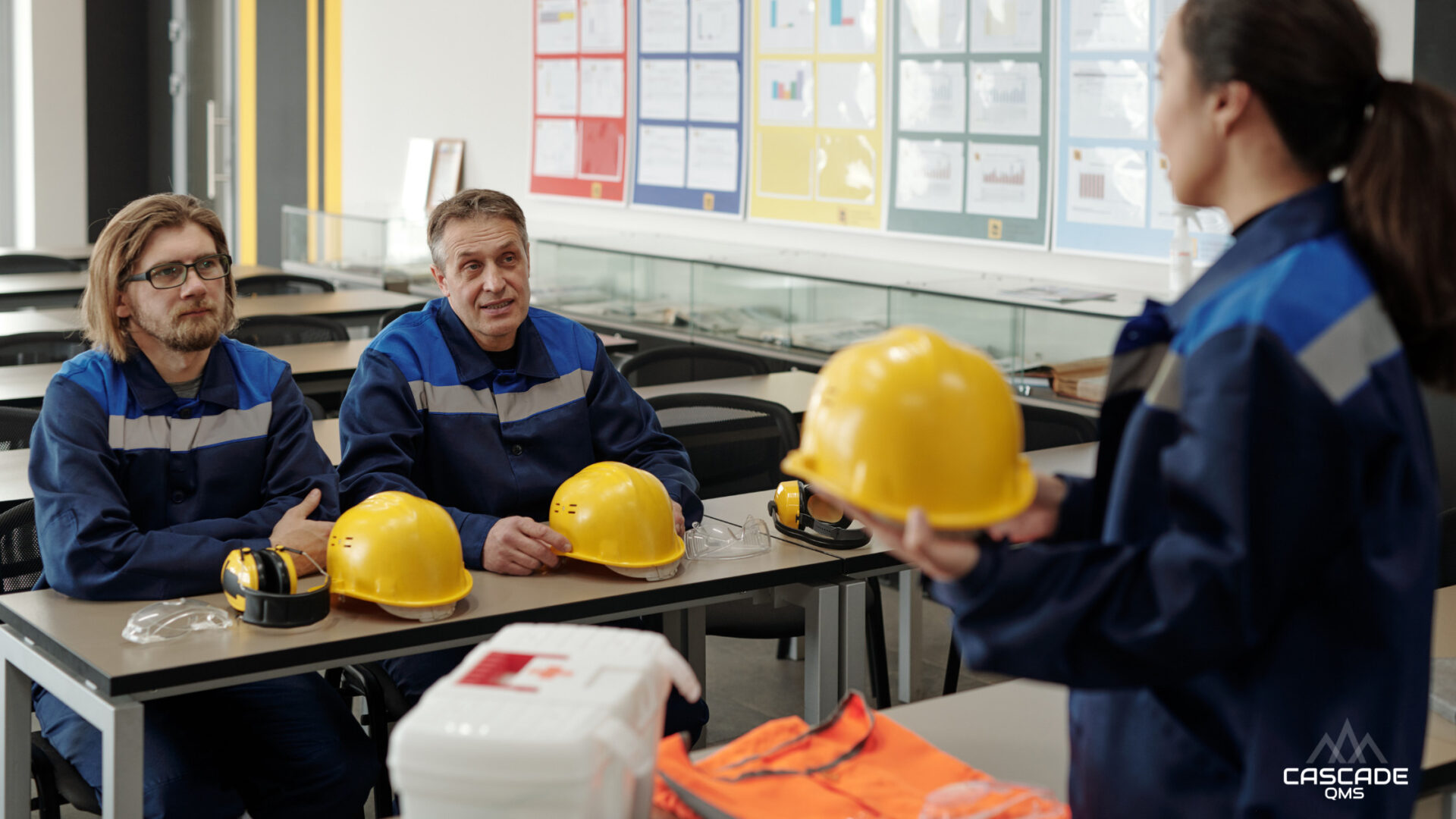 Safety Manager standing infront of two employees discussing PPE RAVS written program in training classroom