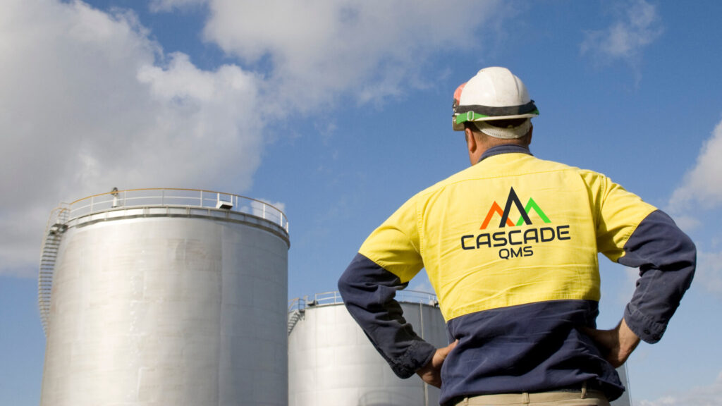 Oil & gas tanks at a refinery with man wearing a hard hat and safety jacket with cascade qms logo